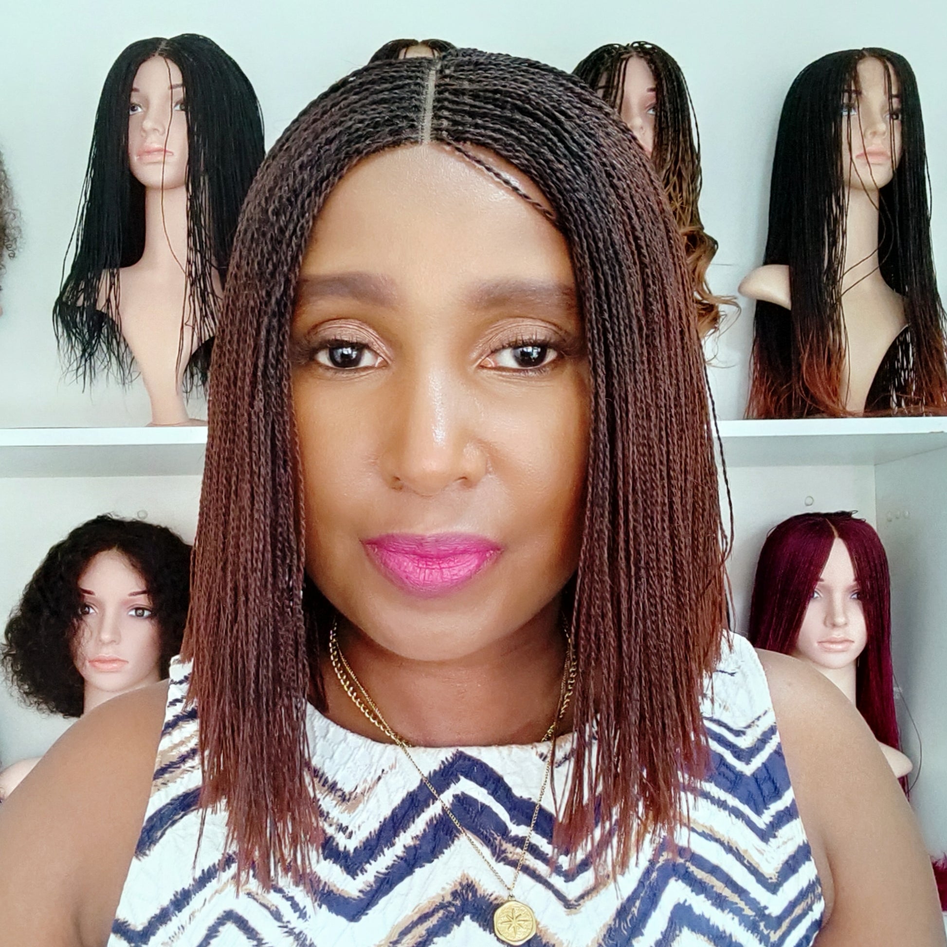 Woman with braided hair in front of mannequin heads with various wigs.